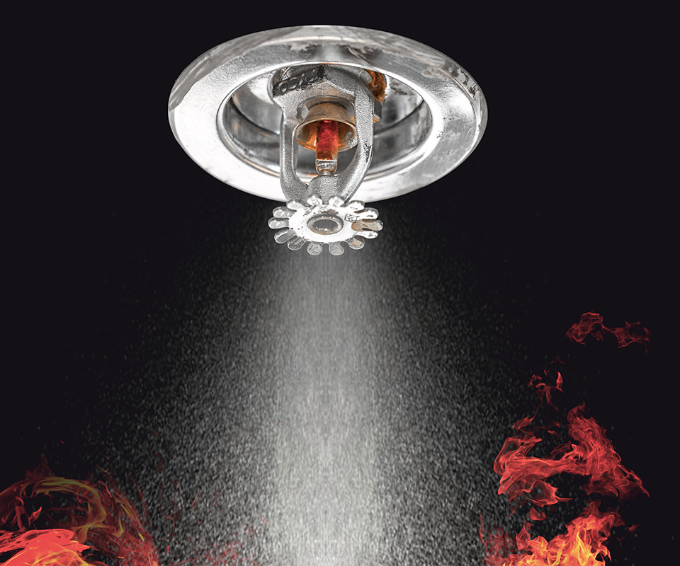 Image of Fire Sprinklers Spraying with fire background. Fire sprinklers are part of an overall safety protocol for fire and life safety.