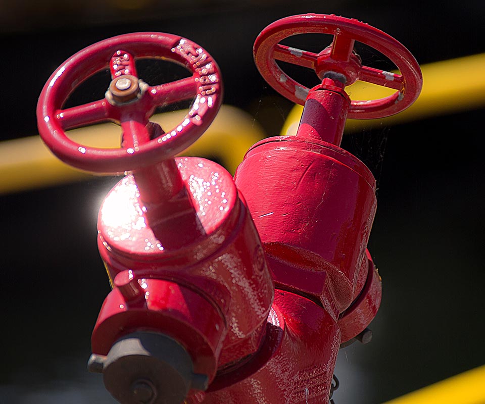 An outdoor red standpipe fire containment system glows in the sunlight.