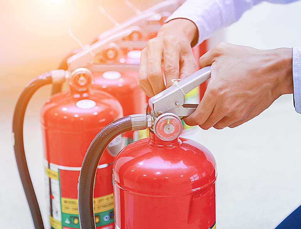 Hand pulling safety pin from red fire extinguisher.